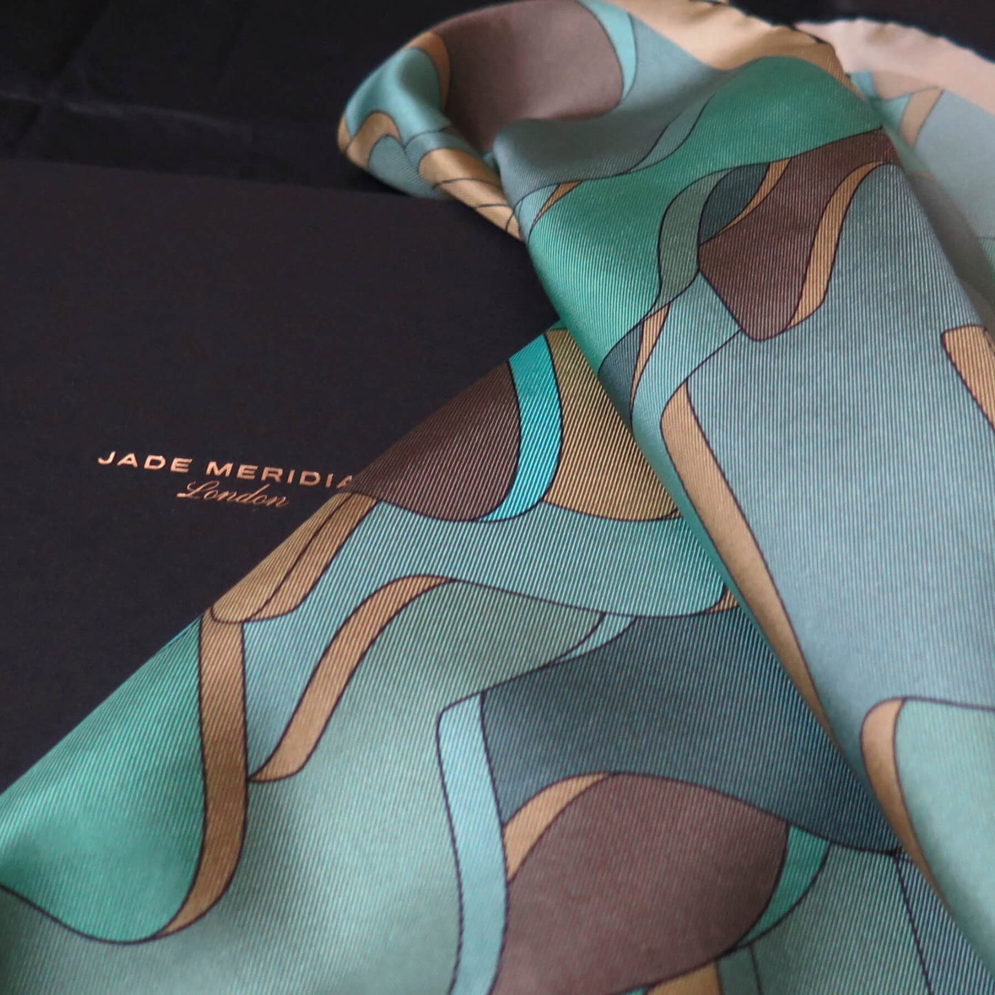 Pure silk scarf with abstract patter in gold, teal, light blue, turquoise and brown on a luxury black gift box with foiled logo