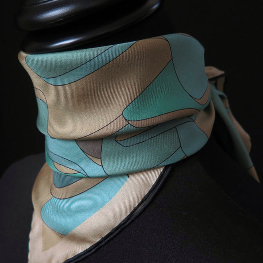 Close up of pure silk scarf with abstract patter in gold, teal, light blue, turquoise and brown, tied in a neckerchief style on a tailors dummy