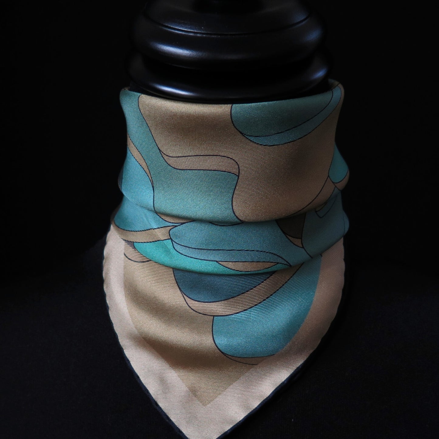 Close up of pure silk scarf with abstract patter in gold, teal, light blue, turquoise and brown, tied in a neckerchief style on a tailors dummy