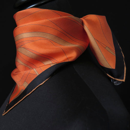 Image of orange and gold pure silk scarf with a dark border and hand-rolled bronze hem. Knotted around the neck, side view