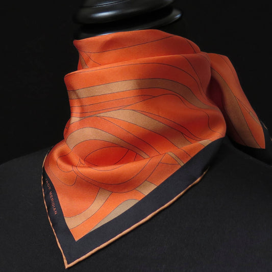 Image of orange and gold pure silk scarf with a dark border and hand-rolled bronze hem. Knotted around the neck, front view