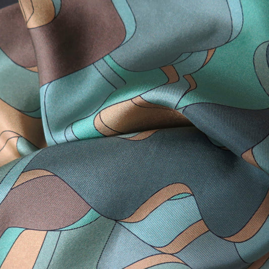 Close up of pure silk scarf with abstract patter in gold, teal, light blue, turquoise and brown