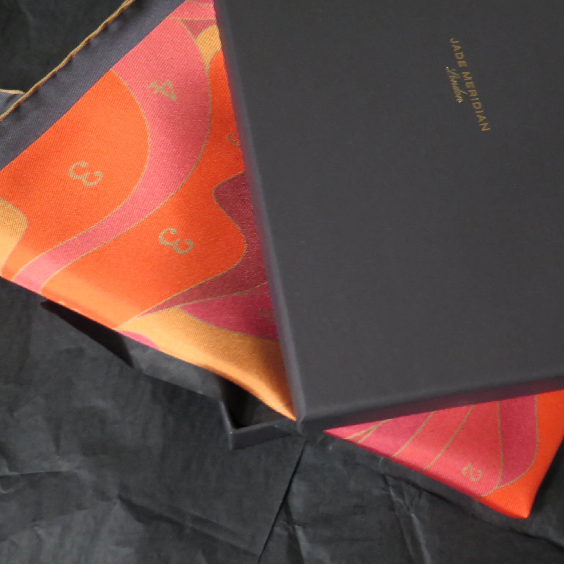Pure silk scarf with a colorful abstract design in a black gift box on a textured surface