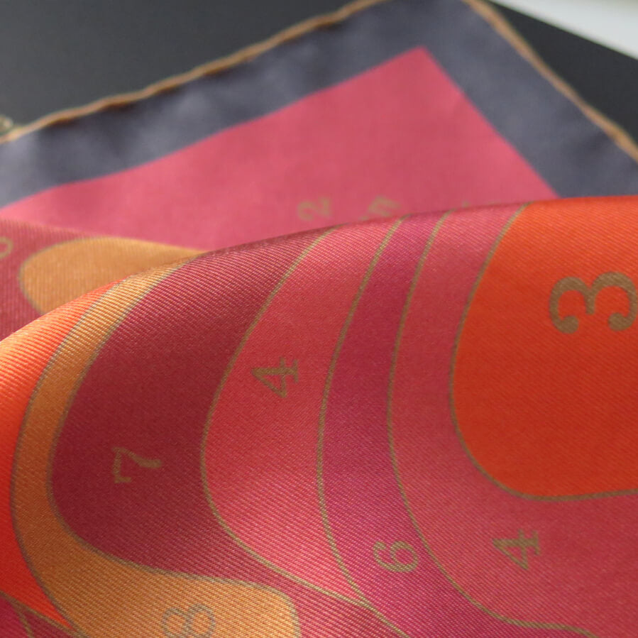 Close-up of a pure silk scarf with orange, pink, ochre and gold patterns on a dark background