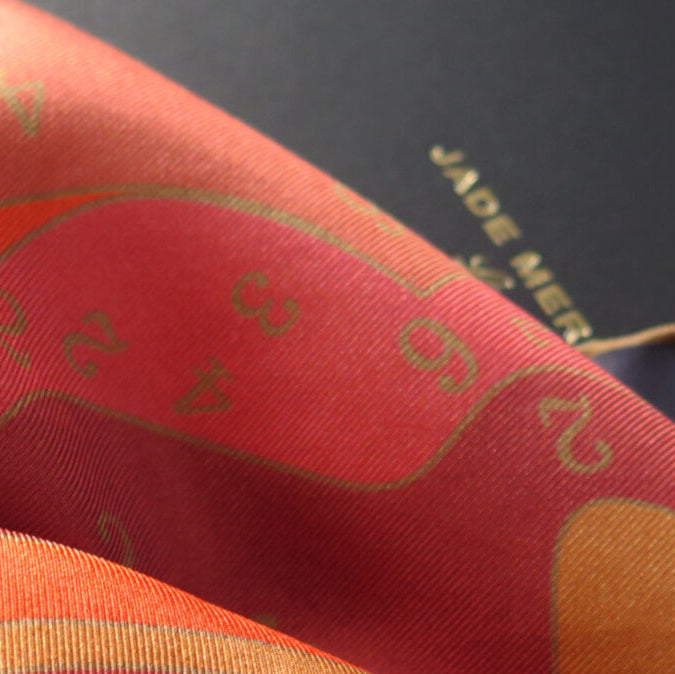 Close-up of a pure silk scarf with orange, ochre, gold and pink pattern.