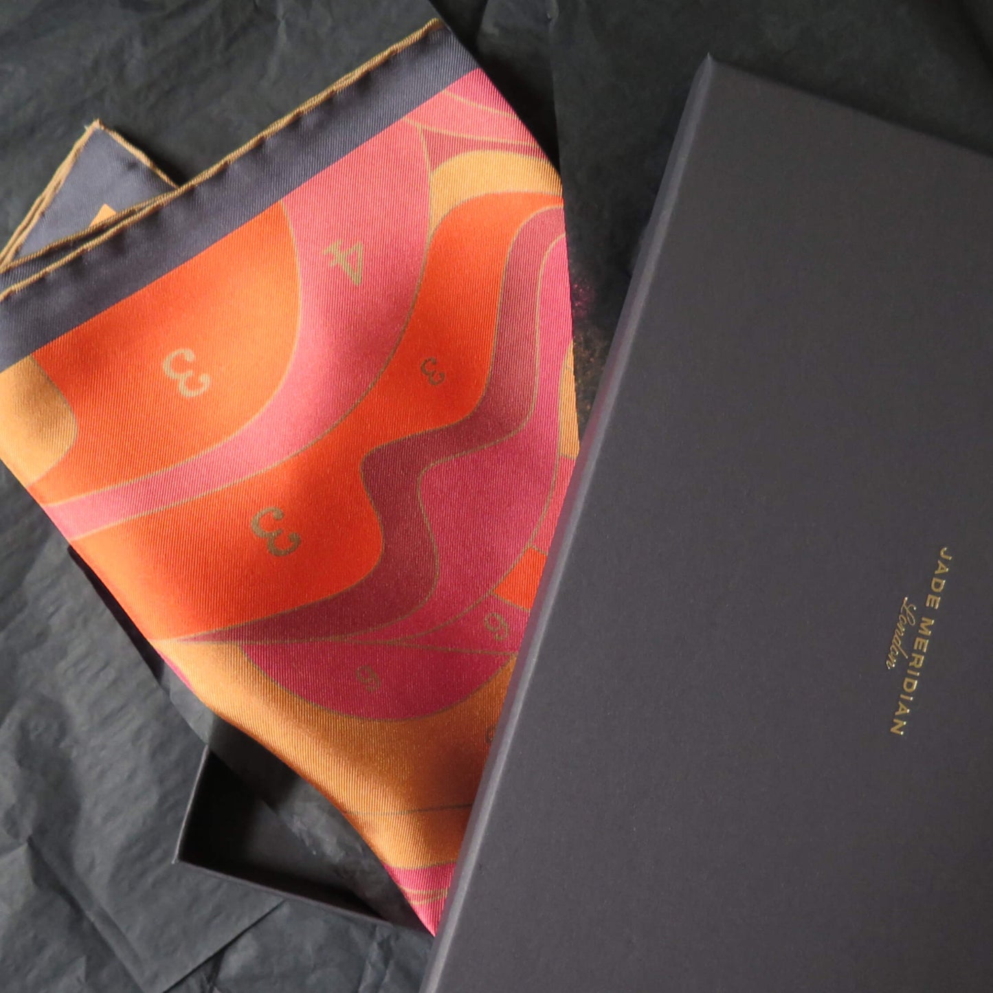 Pure silk scarf with an original colorful abstract design in a black gift box on a textured surface
