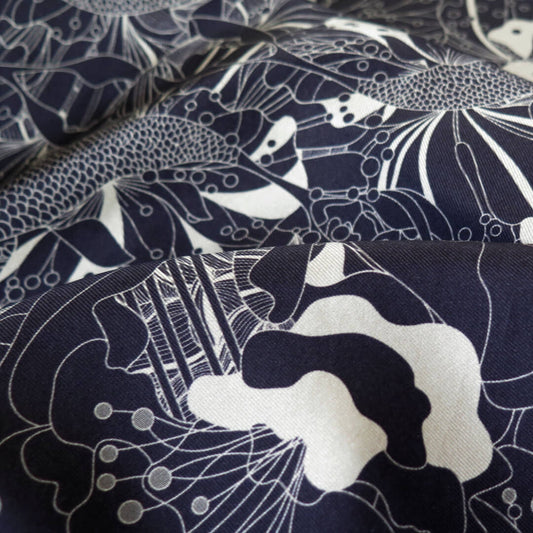 Close up of draped pure silk scarf with hand rolled edge with a deep blue and white gold pattern on a bespoke black gift box with gold foil logo